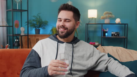 thirsty caucasian man sitting at home holding glass of natural aqua make sips drinking still water