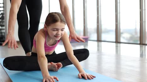 a young girl practices yoga or stretching with an instructor's assistance in a bright studio