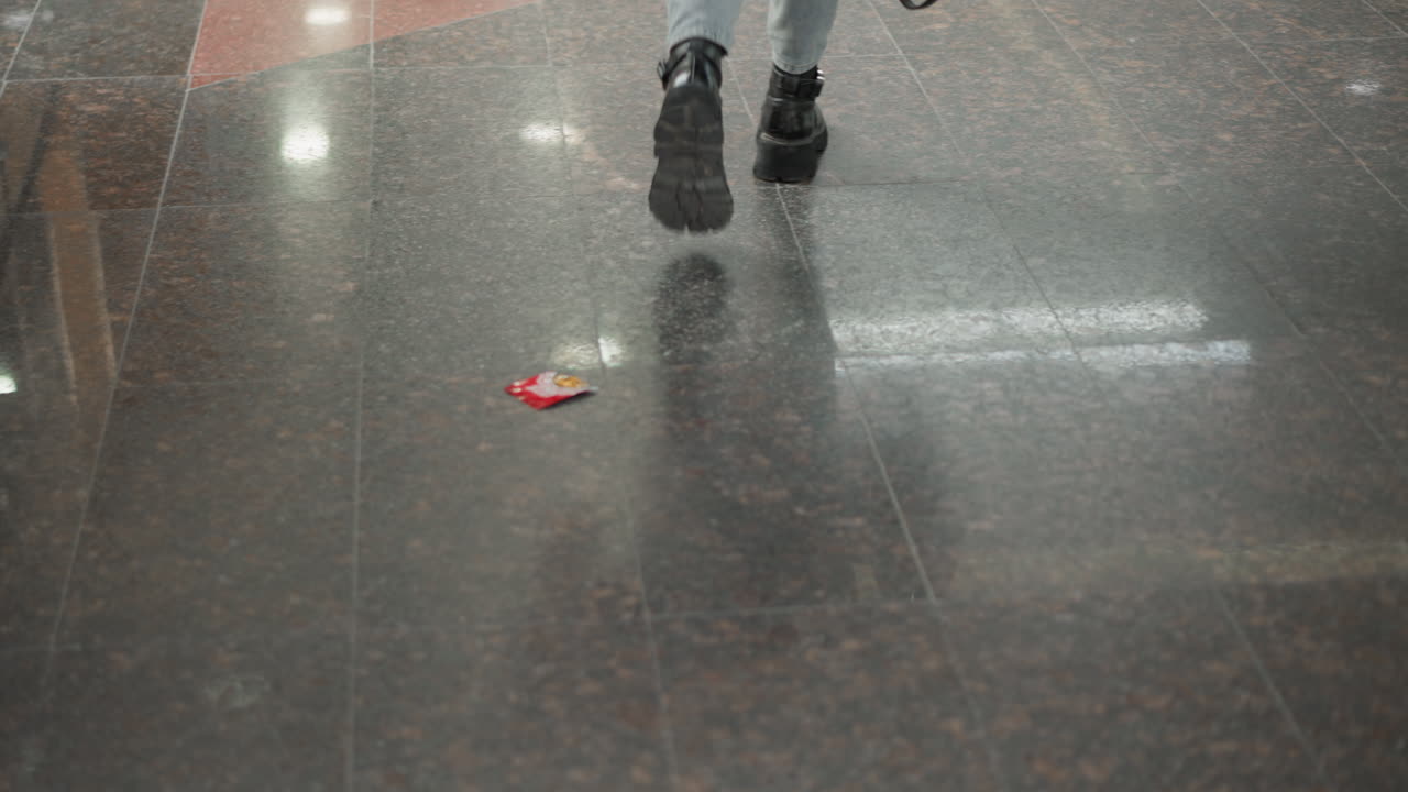 low angle view of woman wearing denim jeans and chunky black boots stepping off moving walkway onto glossy tiled mall floor under bright overhead lights capturing transition from escalator platform