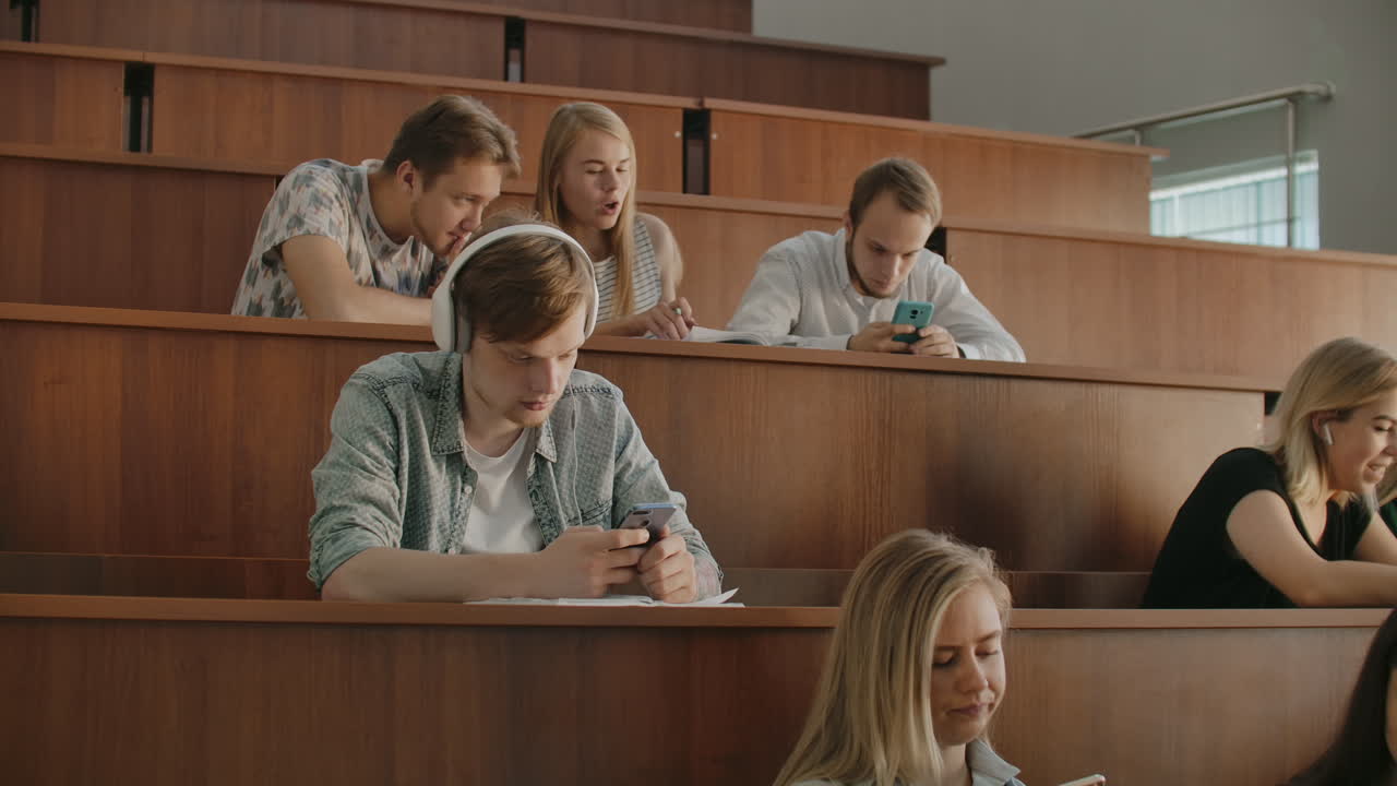 среди большой группы студентов в аудитории человек слушает музыку. слушать музыку и расслабляться. слушать.