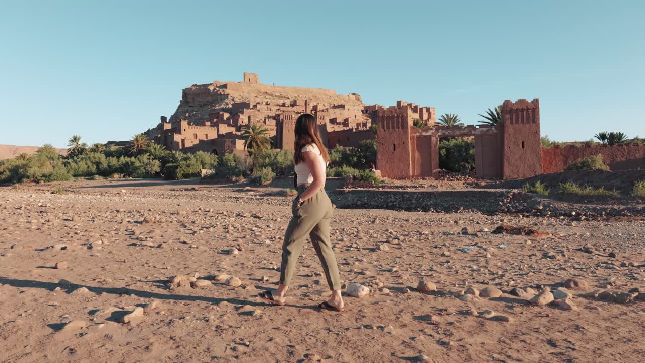 Young caucasian woman walking in front of Ait Ben Haddou fortress in Morocco