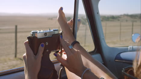 beautiful girl taking photos with vintage camera on road trip in convertible car