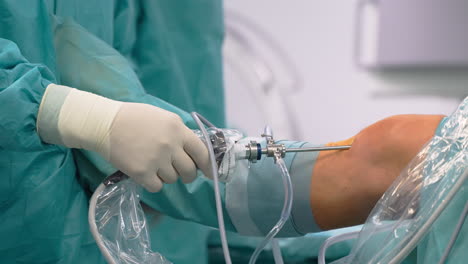 surgeon performing knee arthroscopy operation in hospital with viewing scope instruments inserted into knee joint - close up