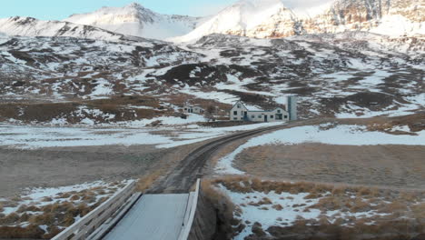 Countryside-of-Iceland,-Aerial-View-of-House-in-Valley-Under-Snowcapped-Volcanic-Hills