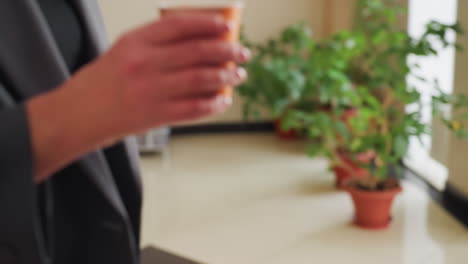 자판기 근처에서 컵을 들고 음료를 고르는 손의 클로즈업, 사무실 환경, 캐주얼한 휴식, 버튼을 누르는 손, 배경에 식물, 음료 선택