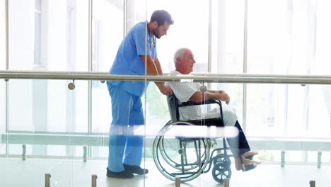 Doctor-holding-senior-patient-on-wheelchair-in-passageway