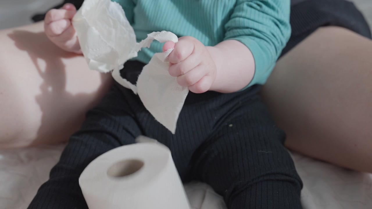 Bebê pega um rolo de papel higiênico da mão da mãe e o rasga de forma divertida.