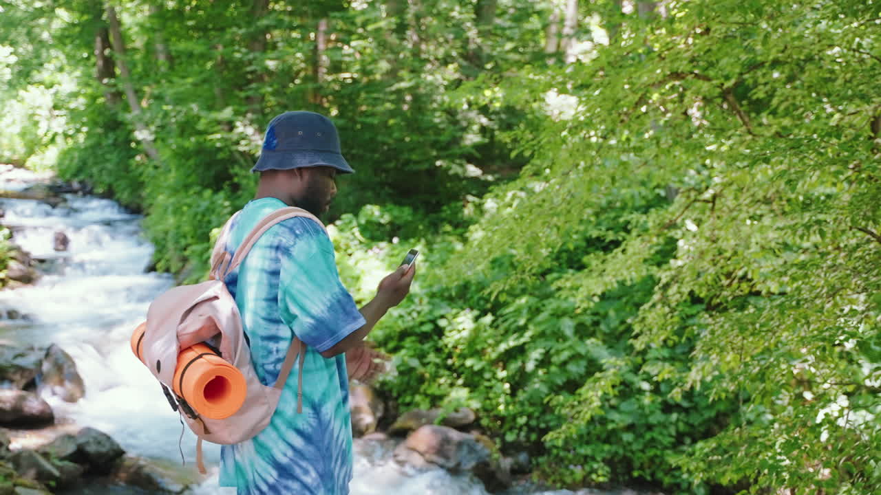 hombre caminando y usando el teléfono en un bosque junto a un arroyo