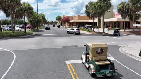a golf cart and cars driving on a road lined with palm trees and buildings.