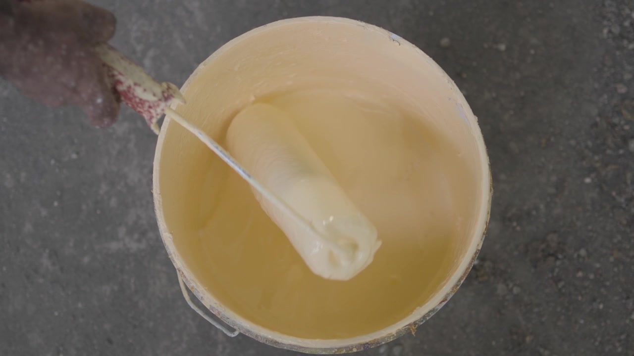 Worker dipping a paint roller into a bucket of fresh wall color, preparing for professional painting and renovation work.