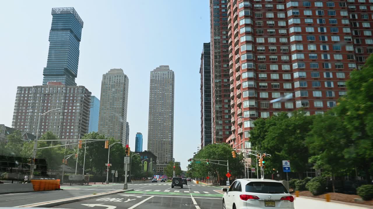 New York, USA, 9 agosto 2025: Grattacieli moderni e verde urbano visti da una strada cittadina. Vista diurna di alti edifici residenziali e per uffici con alberi verdi e traffico su una strada a più corsie.