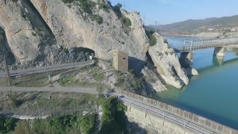 Car-driving-through-tunnel-and-appearing-on-other-side-to-cross-narrow-metal-bridge,-follow-aerial