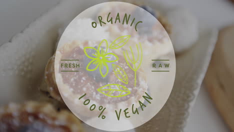 animation of organic 100 percent vegan text over cupcakes in background