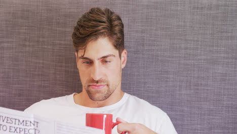 Young-man-sitting-on-bed-having-coffee-while-reading-newspaper-4K-4k