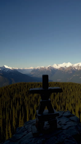 inuksuk silhouette against snow-capped mountains and forest landscape