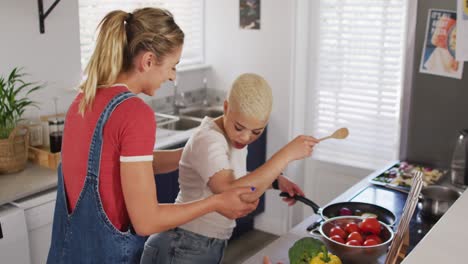 happy diverse female couple cooking vegetables and embracing in kitchen