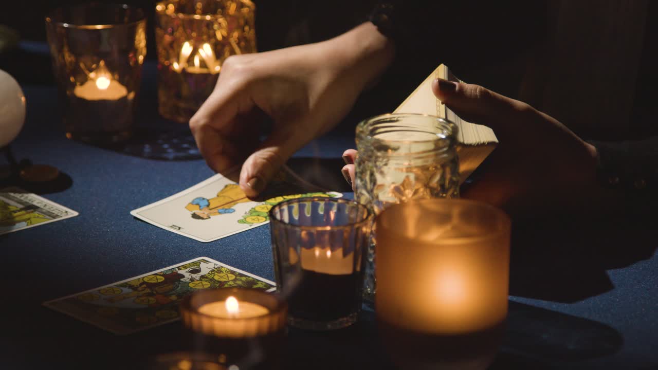 primer plano de una mujer dando lectura de cartas del tarot en una mesa a la luz de las velas sosteniendo la tarjeta de los amantes