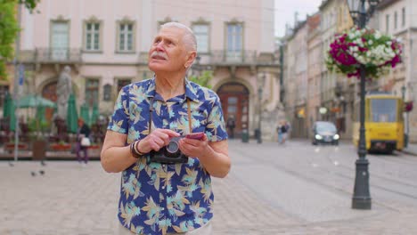 Senior-traveler-man-grandfather-pensioner-getting-lost-in-city,-trying-to-find-route-on-mobile-phone