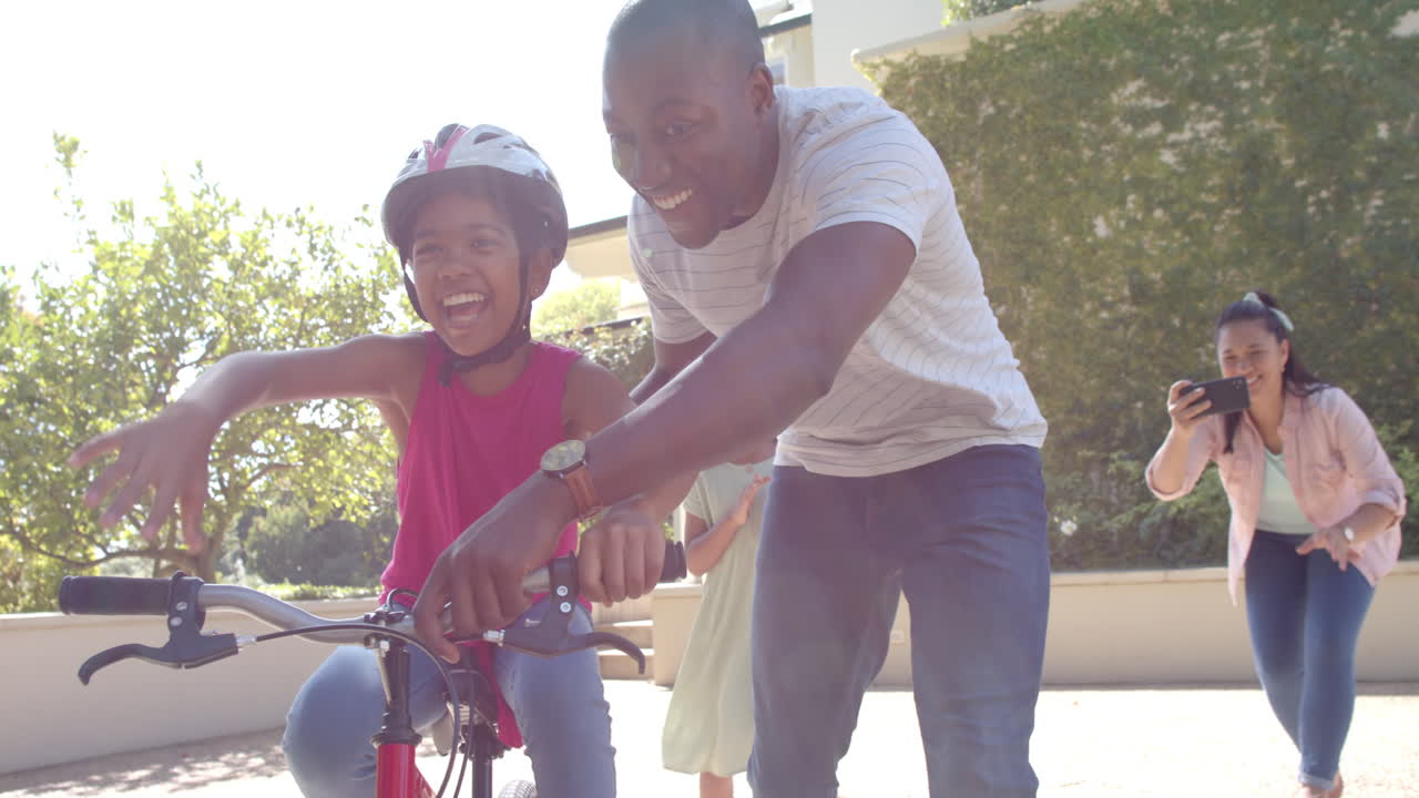 Teaching child to ride bike, father supporting while family cheers and takes photos