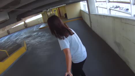 back view of a young woman riding a skateboard down a parking garage