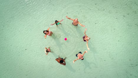 vista aérea de un grupo de amigos en trajes de baño jugando al voleibol en el mar cerca de la playa.
