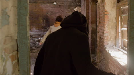 rear view of a man in black balaclava and holding an ax persecuting a redheaded girl in a ruined building 1