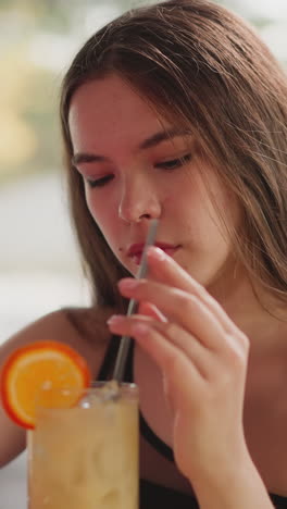 mujer cansada de cabello largo agita cóctel con paja en el bar. señora agotada bebe bebida alcohólica después de una semana de trabajo duro en el bar de la playa. relajación de fin de semana