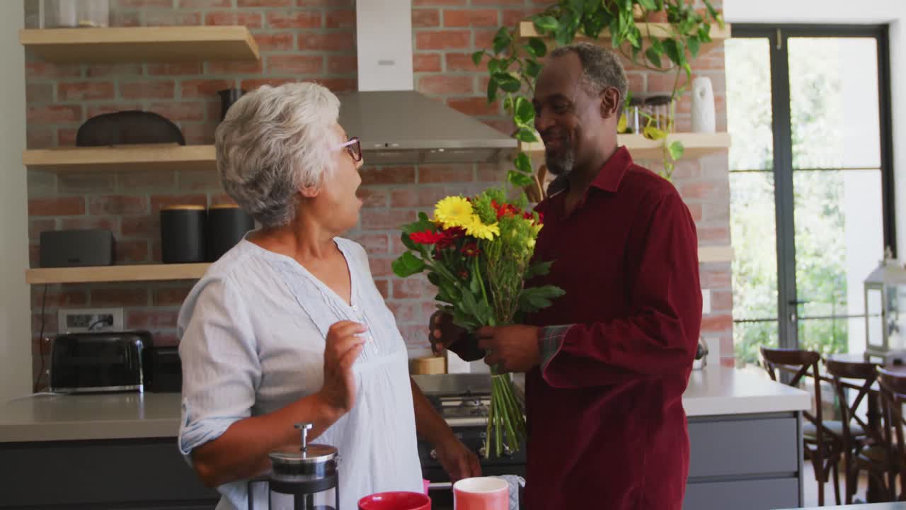 Senior African American husband offering flowers to his wife, hugging and smiling