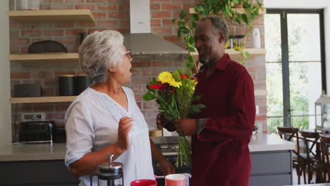 senior african american husband offering flowers to his wife, hugging and smiling