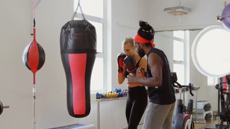 Trainer-assisting-female-boxer-in-fitness-studio-4k