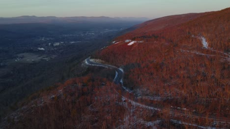 flying over a scenic highway on a mountain high above a vast valley during winter just after sunset, with a little snow on the ground