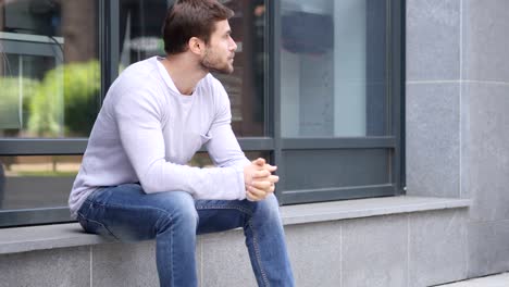 un hombre guapo y serio sentado fuera de la oficina y mirando a su alrededor