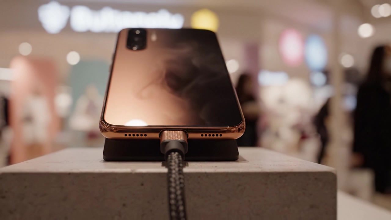 Nabíjení mobilního telefonu na dokovací stanici v prostředí obchodu se stylovým designem a jemným rozostřením pozadí, které zdůrazňuje modernost a pohodlí technologie