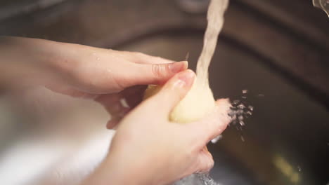 부엌 수도꼭지에서 물 아래 양파를 씻는 여성 손의 슬로우 모션 샷