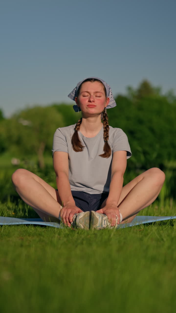 A Gen Z woman sits in a peaceful park, settles into a calm posture, practices breathwork, and smiles with inner joy. Soft vertical 4K dolly shot capturing mindful serenity in nature