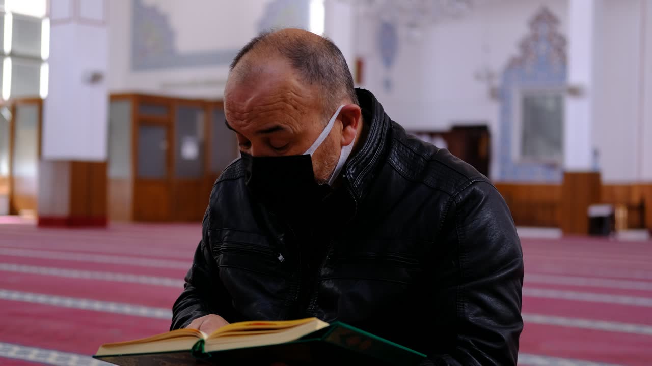 남자는 마스크를 쓰고 모스크에서 꾸란을 읽습니다.