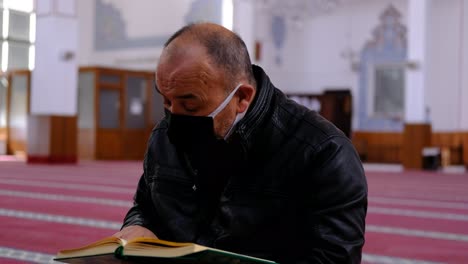 man wears mask and reads the quran in mosque