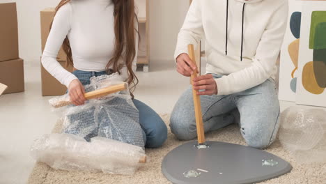 close up of unrecognizable couple moving into new house sitting on floor and assembling coffee table together