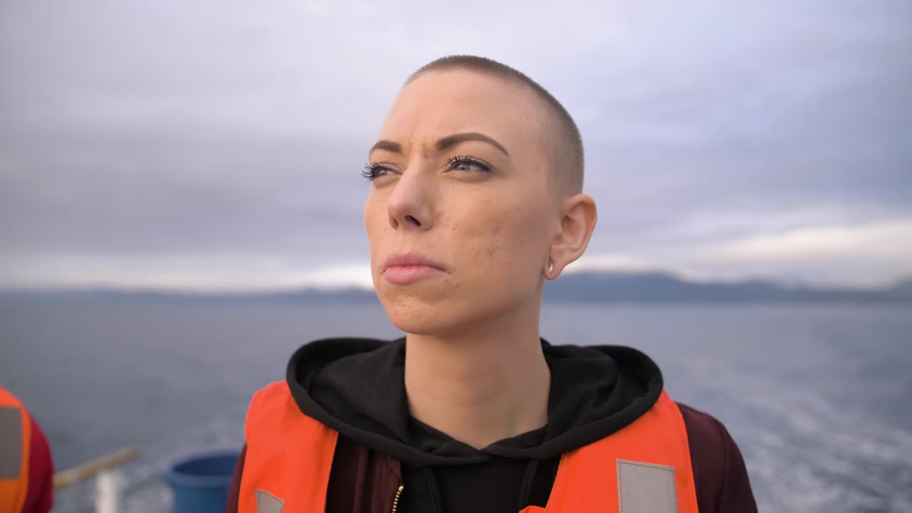 Rallentatore, vista ravvicinata di una donna con la testa rasata che indossa un giubbotto di salvataggio mentre è su una barca in movimento