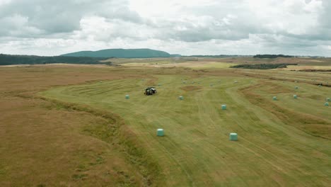 field full of round hay bales with tractor machine for haybale making, aerial