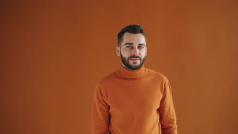 man in orange sweater making a silence gesture