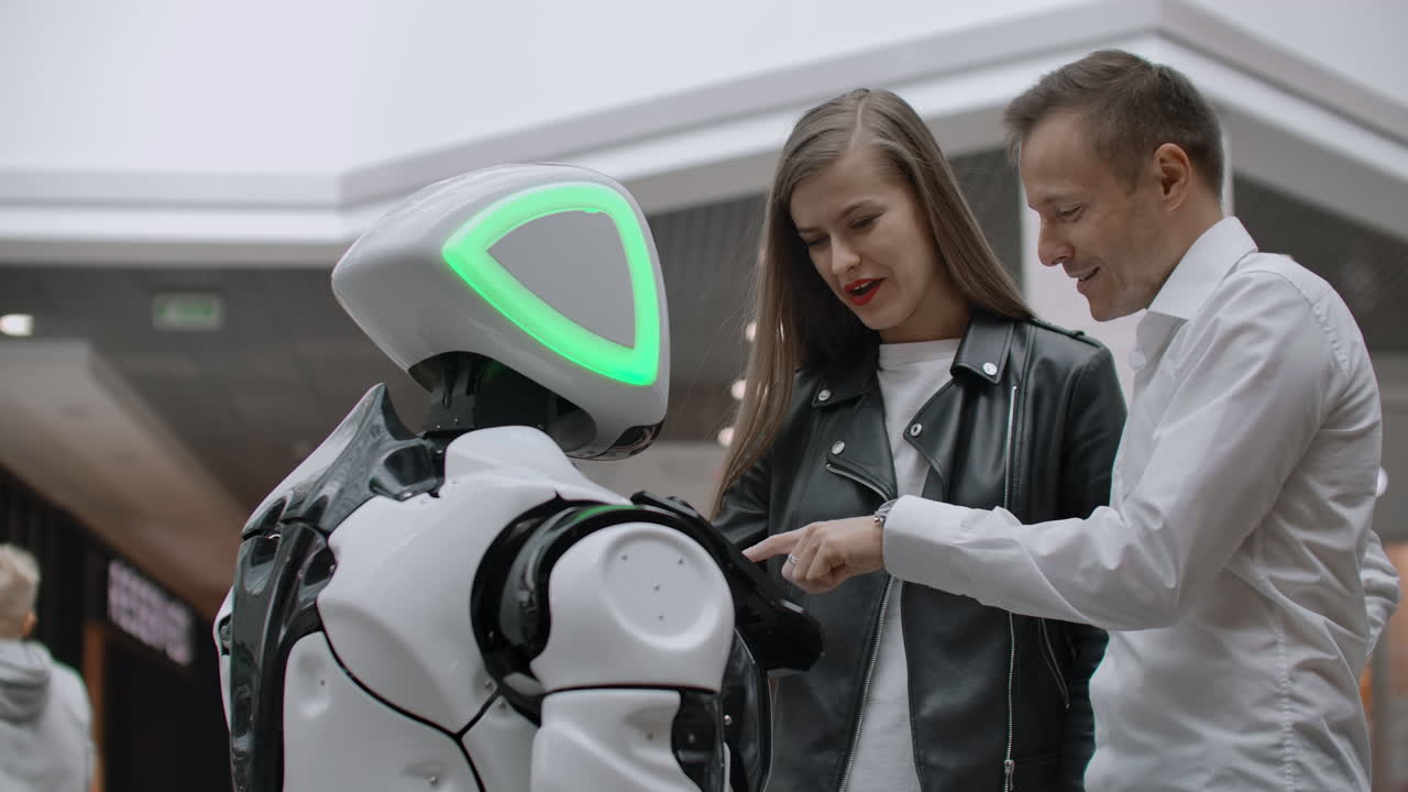 un hombre y una mujer en el centro comercial interactúan con un consultor robot tocando la pantalla y sonriendo. cyborg android ayuda a la gente