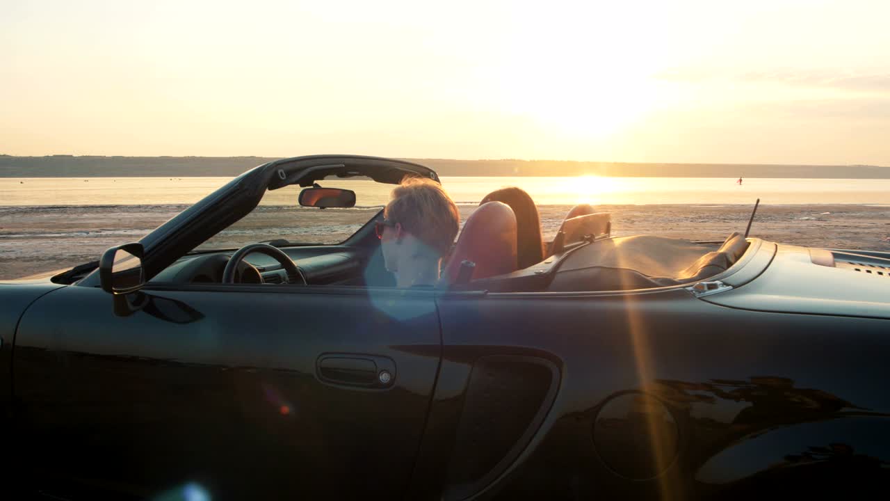 una joven pareja feliz conduciendo en un cabriolet durante la puesta de sol, en cámara lenta.