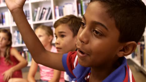 Schoolboy-raising-hand-in-library