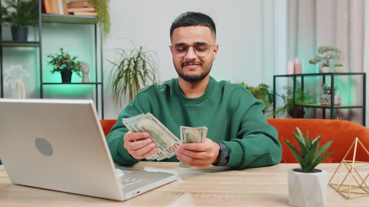 Hombre feliz sonriente contando dinero en efectivo y usar computadora portátil calcular las ganancias de los ingresos domésticos en casa