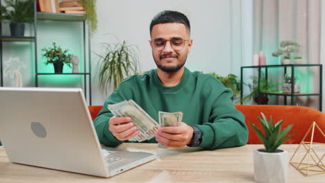 hombre feliz sonriente contando dinero en efectivo y usar computadora portátil calcular los ingresos domésticos ganancias en casa