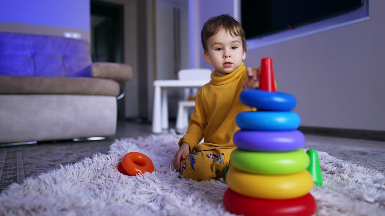 Cute Caucasian toddler in yellow pajama sitting on the fluffy plaid. Little boy plays with toy pyramid.