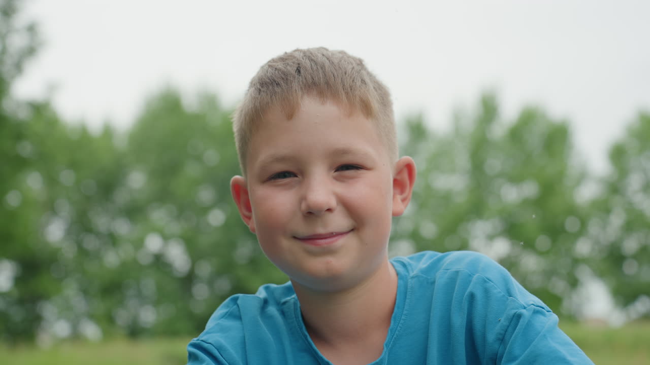 Giovane ciclista sorridente, bambino che si gode una gita nel verde, ragazzino allegro in bicicletta tra gli alberi alla luce del giorno, bambino felice che pedala attraverso un campo aperto con alberi frondosi sullo sfondo