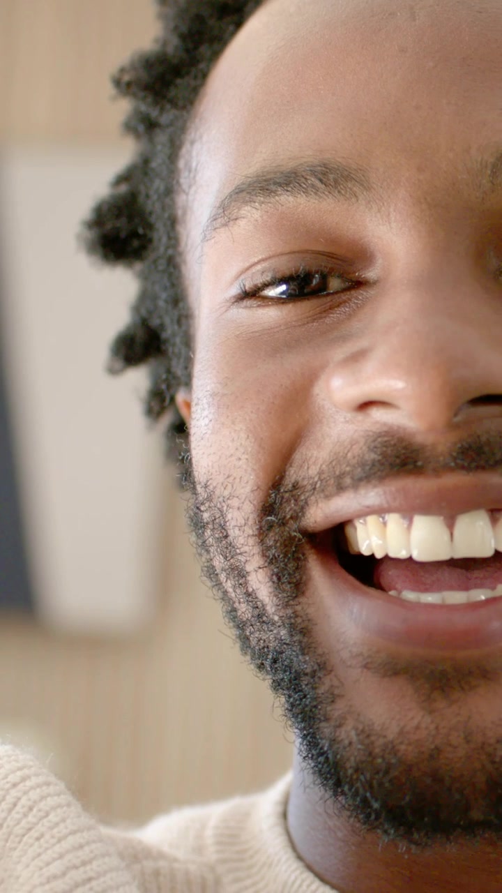 Vertical video: Smiling, man in cream sweater leaning, reaching phone at home to block camera lens