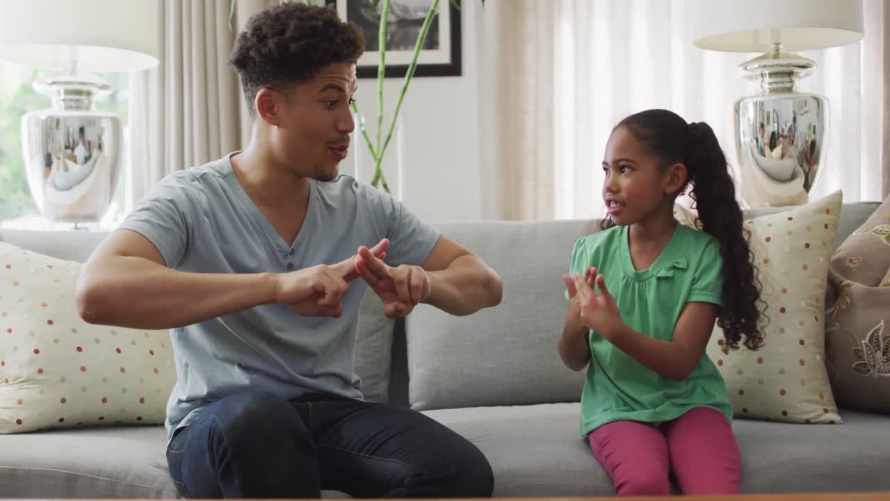 Happy biracial father and daughter sitting on sofa using sign language